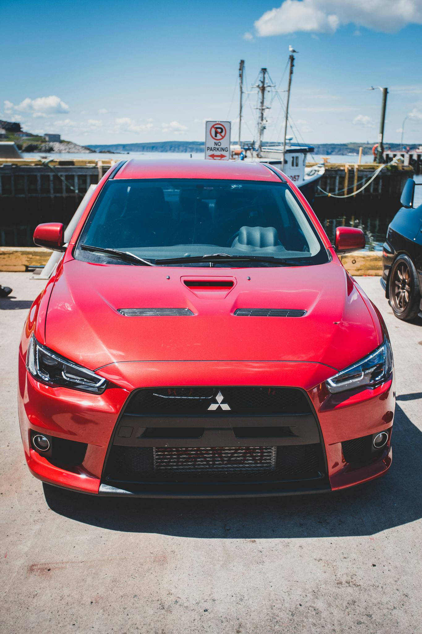 A vibrant red Mitsubishi car parked by the pier on a sunny day.