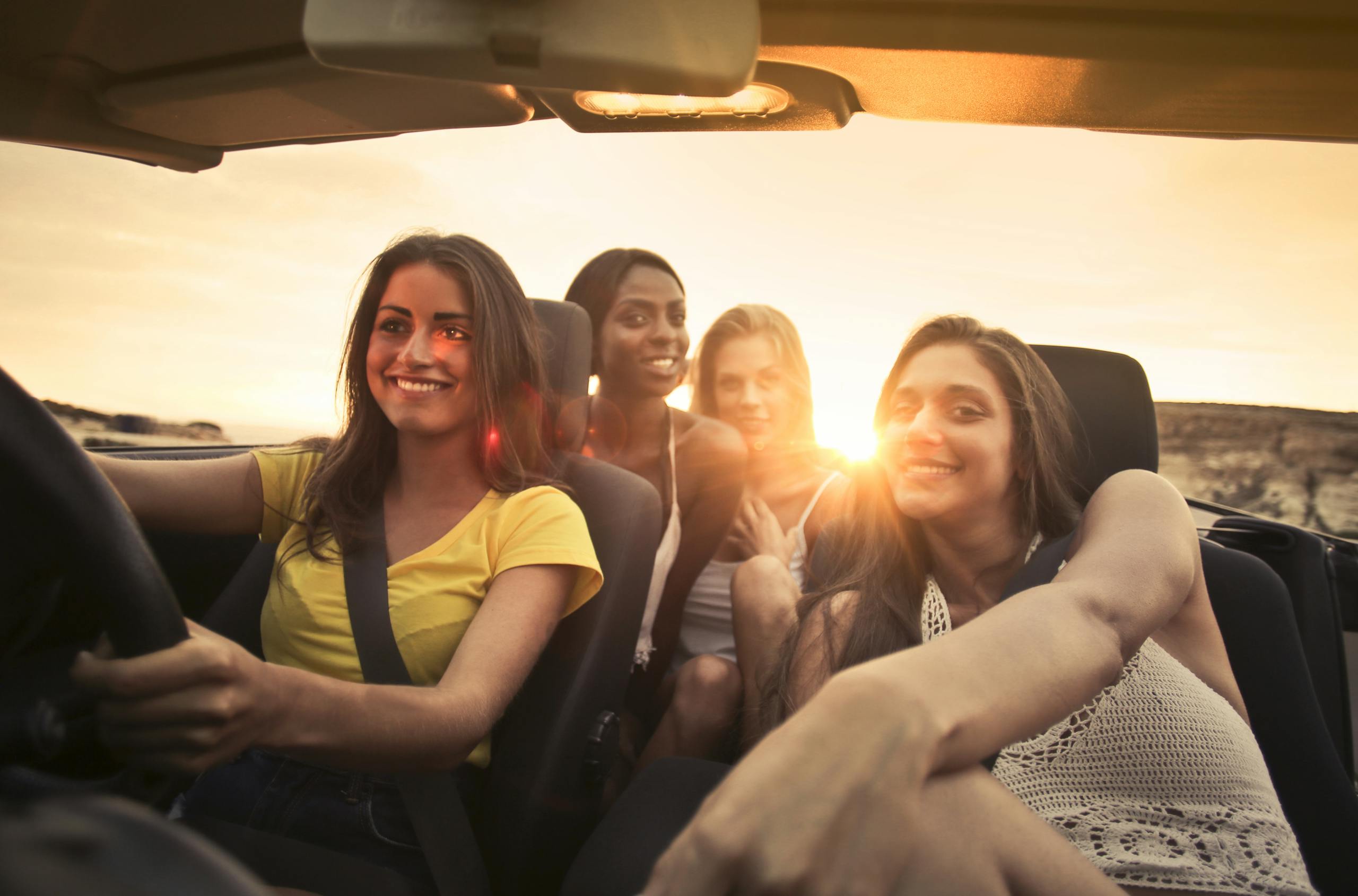 Four friends share smiles and laughter in a convertible during a sunset road trip in